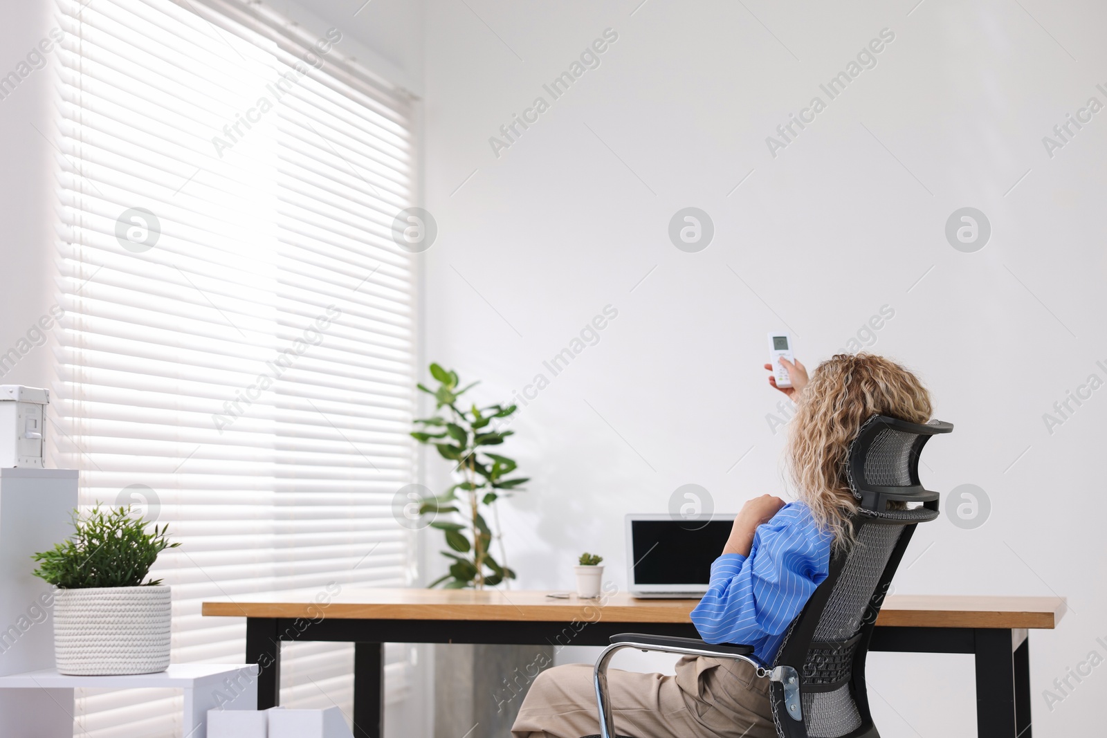 Woman using remote to control air conditioner in office, back view Photo of Woman using remote to control air conditioner in office, back view
