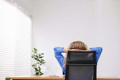 Photo of Woman sitting at workplace in office with air conditioning, back view