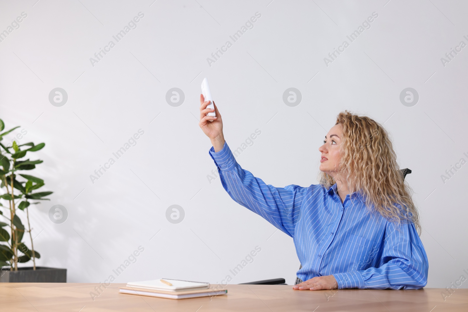Woman using remote to control air conditioner in office Photo of Woman using remote to control air conditioner in office
