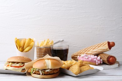Photo of Different delicious fast food and cola on light wooden table against white background, closeup