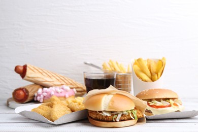 Photo of Different delicious fast food and cola on light wooden table against white background, closeup