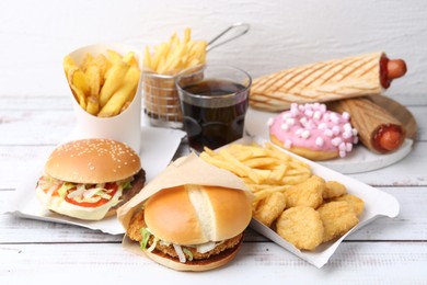 Photo of Different delicious fast food and cola on light wooden table, closeup