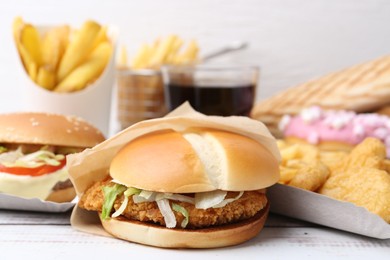 Photo of Different delicious fast food on light wooden table, closeup
