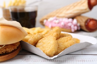 Photo of Different delicious fast food on light wooden table, closeup