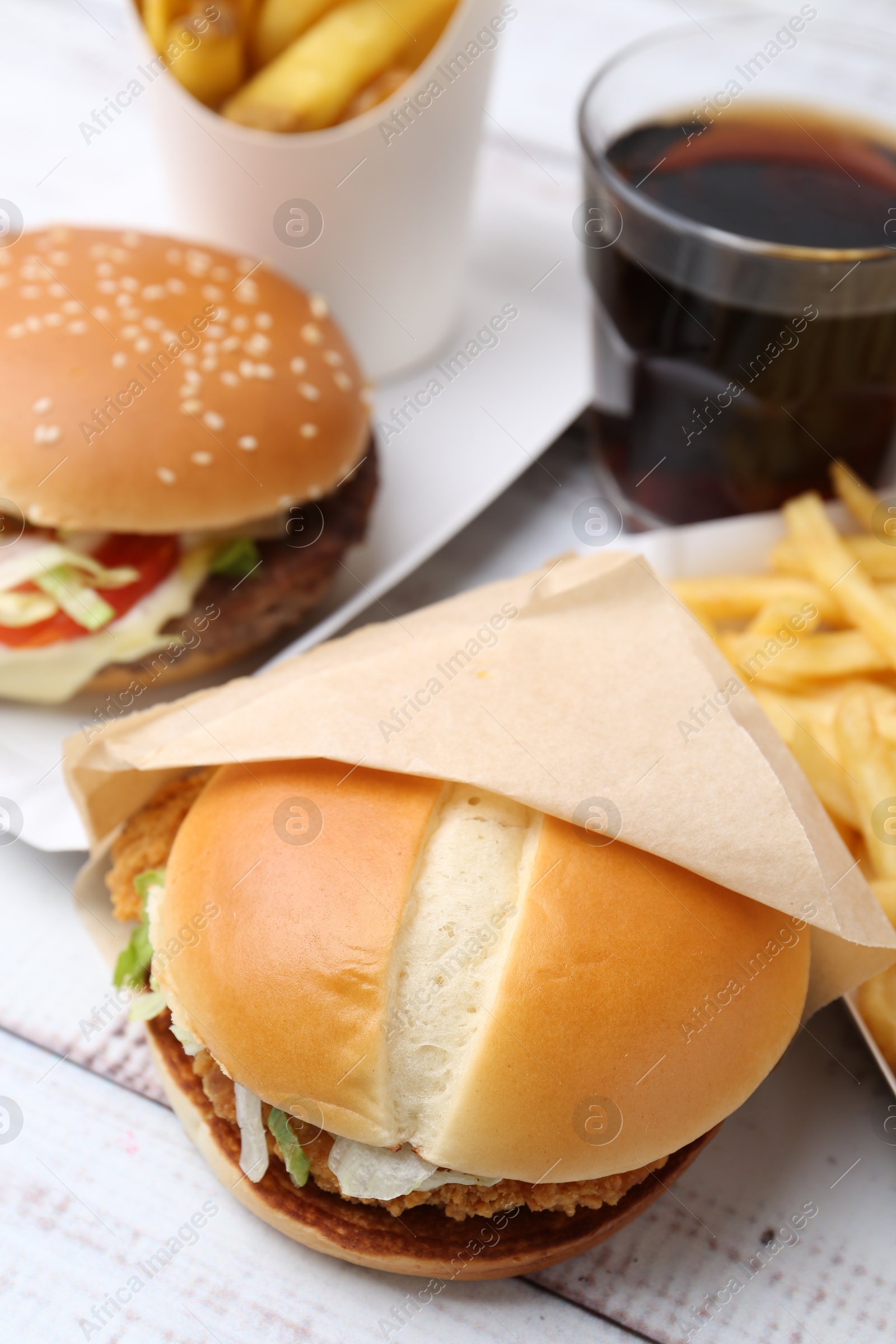 Delicious burgers and cola on light wooden table, closeup. Tasty fast food Photo of Delicious burgers and cola on light wooden table, closeup. Tasty fast food