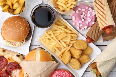 Photo of Different delicious fast food and cola on light wooden table, flat lay