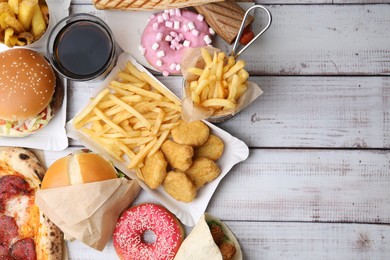 Photo of Different delicious fast food and cola on light wooden table, flat lay. Space for text