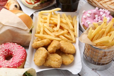 Photo of Different delicious fast food on light wooden table, closeup