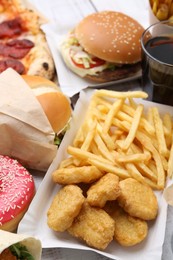 Photo of Different delicious fast food on light wooden table, closeup
