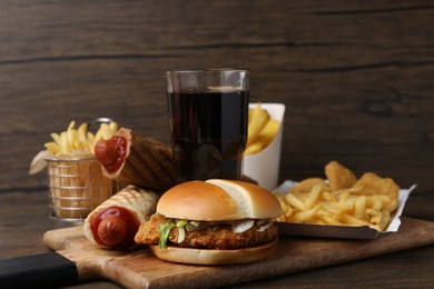 Photo of Different delicious fast food and cola on wooden table, closeup
