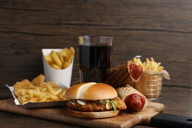 Photo of Different delicious fast food and cola on wooden table, closeup