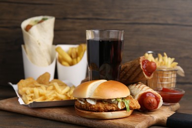Photo of Different delicious fast food and cola on wooden table, closeup