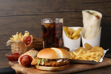 Photo of Different delicious fast food and cola on wooden table, closeup