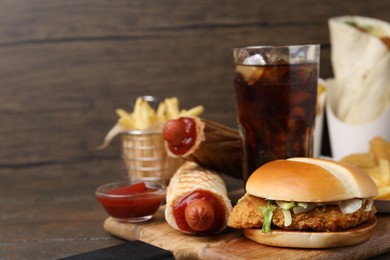 Photo of Delicious burger, cola and other fast food on wooden table, closeup. Space for text