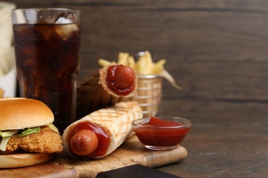 Photo of Delicious burger, cola and other fast food on wooden table, closeup. Space for text