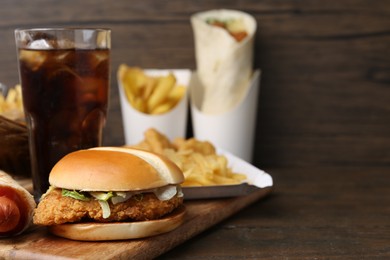 Photo of Delicious burger, cola and other fast food on wooden table, closeup. Space for text