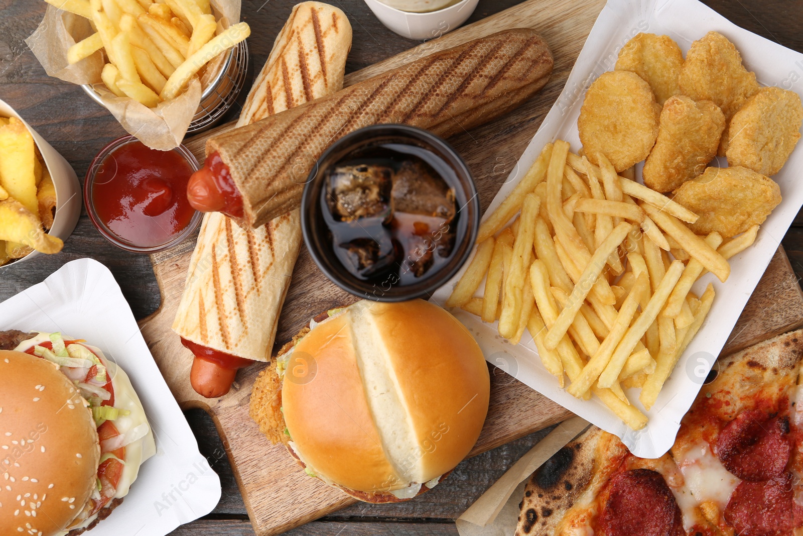 Different delicious fast food and cola on wooden table, flat lay Photo of Different delicious fast food and cola on wooden table, flat lay