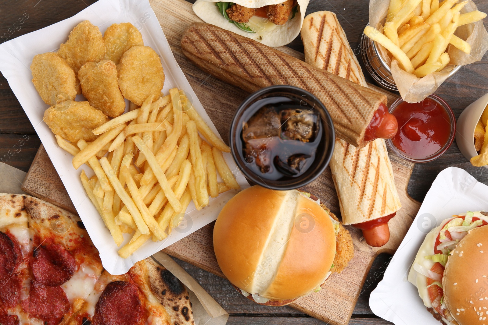 Different delicious fast food and cola on wooden table, flat lay Photo of Different delicious fast food and cola on wooden table, flat lay