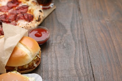 Photo of Delicious burger, ketchup and pizza on wooden table, closeup with space for text. Tasty fast food