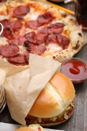 Photo of Delicious burger, ketchup and pizza on wooden table, closeup. Tasty fast food