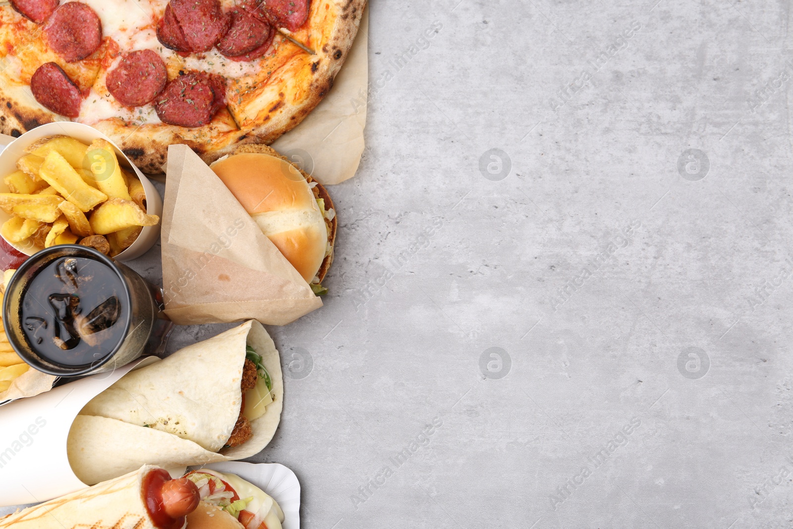 Different delicious fast food and cola on light grey textured table, flat lay. Space for text Photo of Different delicious fast food and cola on light grey textured table, flat lay. Space for text