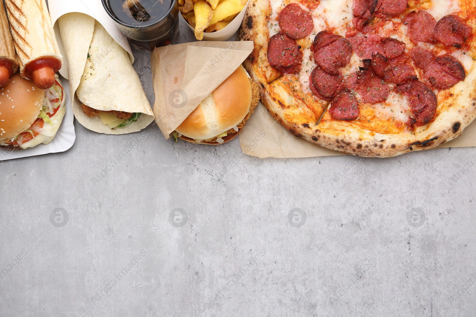 Different delicious fast food and cola on light grey textured table, flat lay. Space for text Photo of Different delicious fast food and cola on light grey textured table, flat lay. Space for text