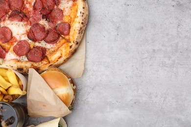 Photo of Different delicious fast food and cola on light grey textured table, flat lay. Space for text