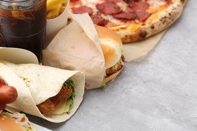 Photo of Different delicious fast food and cola on light grey textured table, closeup