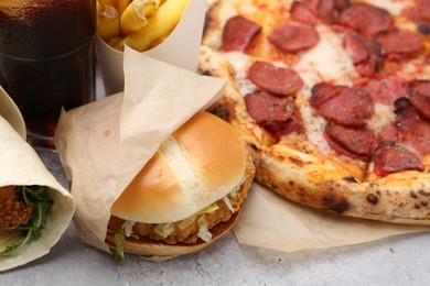 Photo of Different delicious fast food on light grey textured table, closeup