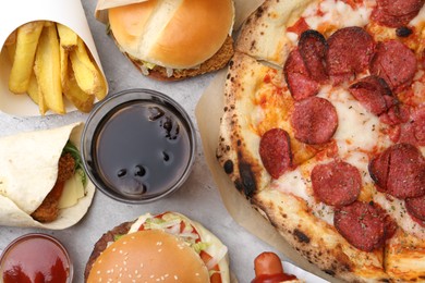 Photo of Different delicious fast food and cola on light grey textured table, flat lay