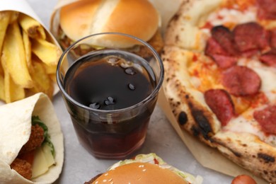 Photo of Different delicious fast food and cola on light grey textured table, closeup