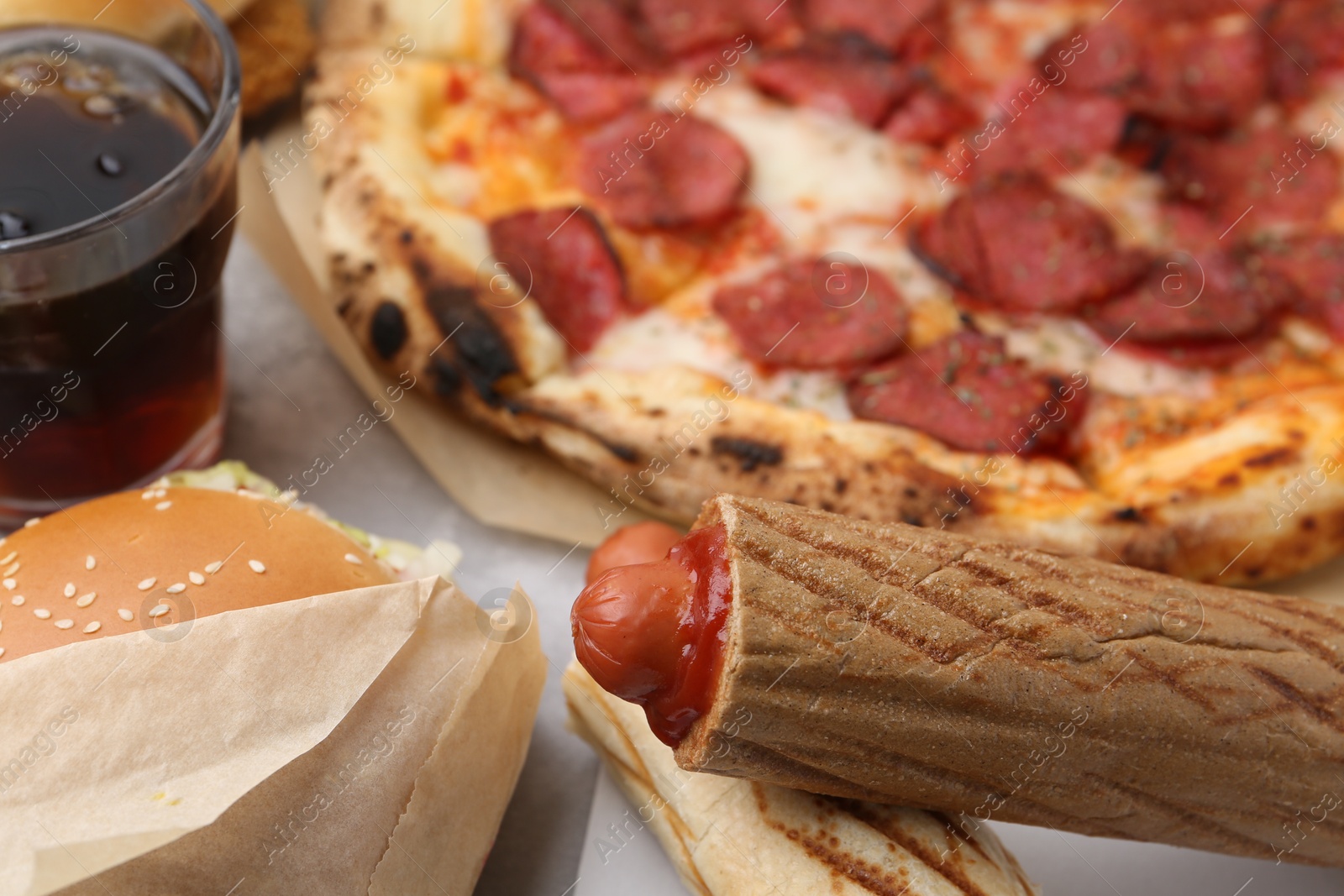 Delicious hot dogs, burger, pizza and cola on light table, closeup. Tasty fast food Photo of Delicious hot dogs, burger, pizza and cola on light table, closeup. Tasty fast food