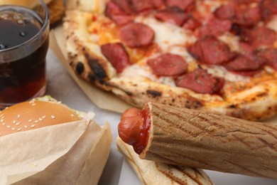 Photo of Delicious hot dogs, burger, pizza and cola on light table, closeup. Tasty fast food