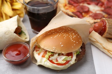 Photo of Delicious burger, ketchup and other fast food on grey textured table, closeup