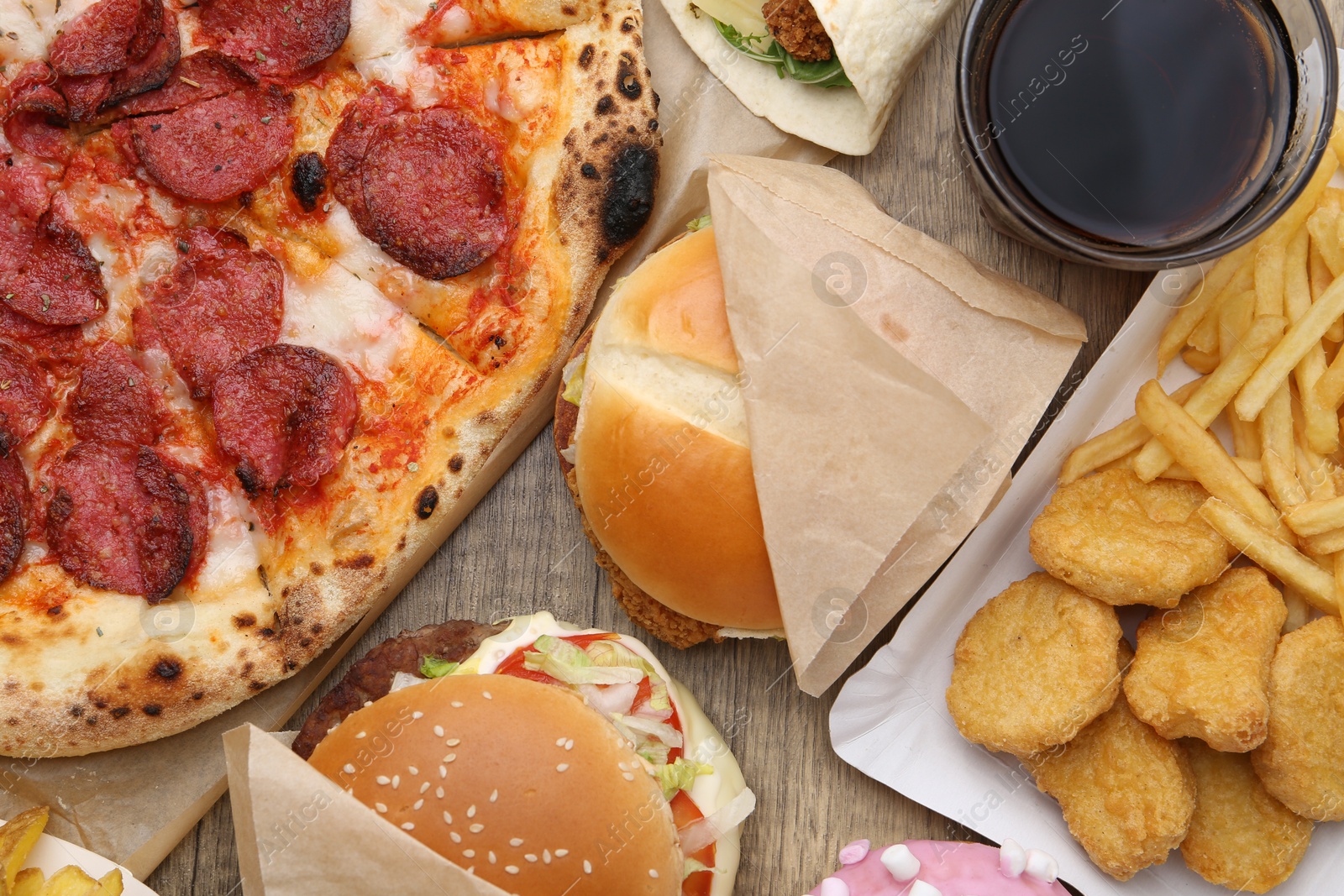 Different delicious fast food and cola on wooden table, flat lay Photo of Different delicious fast food and cola on wooden table, flat lay
