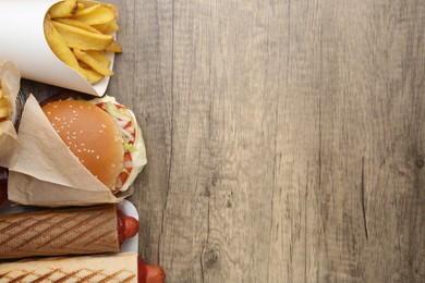 Photo of Different delicious fast food on wooden table, flat lay. Space for text