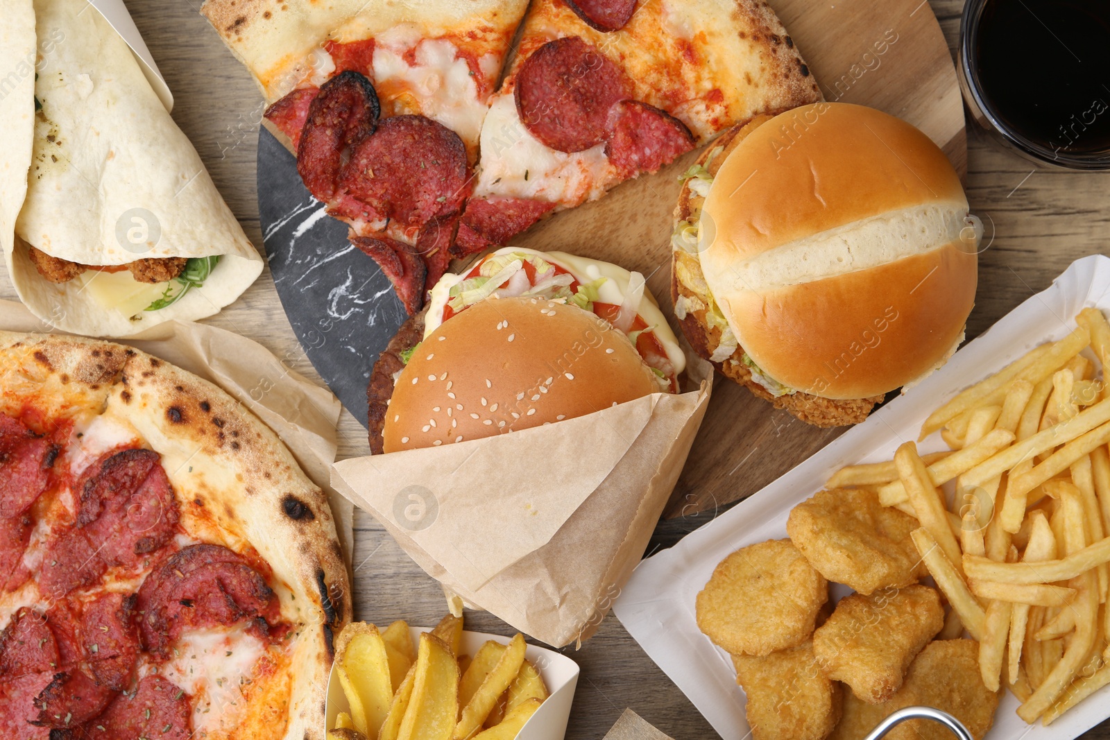 Different delicious fast food and cola on wooden table, flat lay Photo of Different delicious fast food and cola on wooden table, flat lay