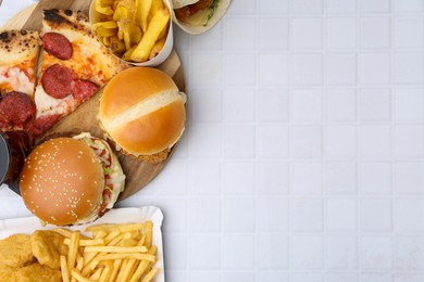Photo of Different delicious fast food on white tiled table, flat lay. Space for text