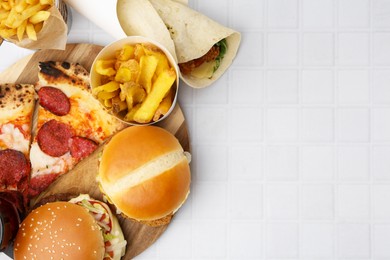 Photo of Different delicious fast food on white tiled table, flat lay. Space for text