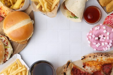 Photo of Frame of different delicious fast food, ketchup and cola on white tiled table, flat lay. Space for text