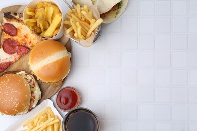 Photo of Different delicious fast food, ketchup and cola on white tiled table, flat lay. Space for text