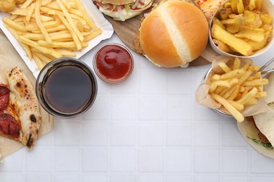 Photo of Different delicious fast food, ketchup and cola on white tiled table, flat lay. Space for text