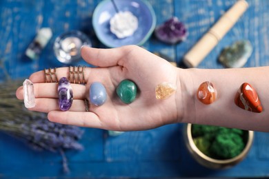 Photo of Woman with chakra gemstones at blue wooden table, closeup