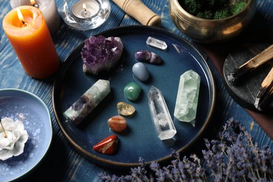 Photo of Chakra gemstones, lavender flowers, incense and burning candles on blue wooden table, closeup