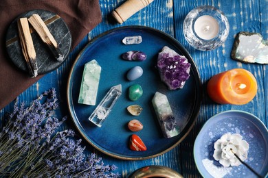 Photo of Chakra gemstones, lavender flowers, incense, palo santo and burning candles on blue wooden table, flat lay