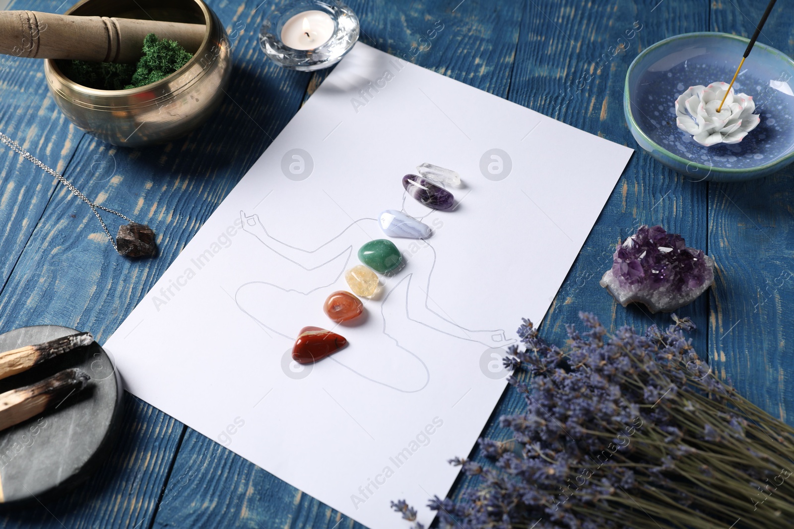 Human drawing with gemstones placed on chakras, lavender flowers, incense and palo santo on blue wooden table Photo of Human drawing with gemstones placed on chakras, lavender flowers, incense and palo santo on blue wooden table