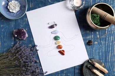Photo of Human drawing with gemstones placed on chakras, lavender flowers, incense and palo santo on blue wooden table, flat lay