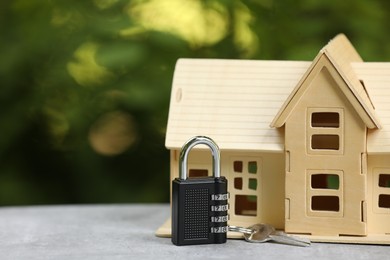 Photo of Home security. House model, key and padlock on light grey table outdoors, closeup. Space for text