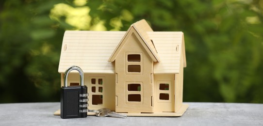 Photo of Home security. House model, key and padlock on light grey table outdoors, closeup