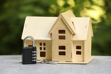 Photo of Home security. House model, key and padlock on light grey table outdoors, closeup